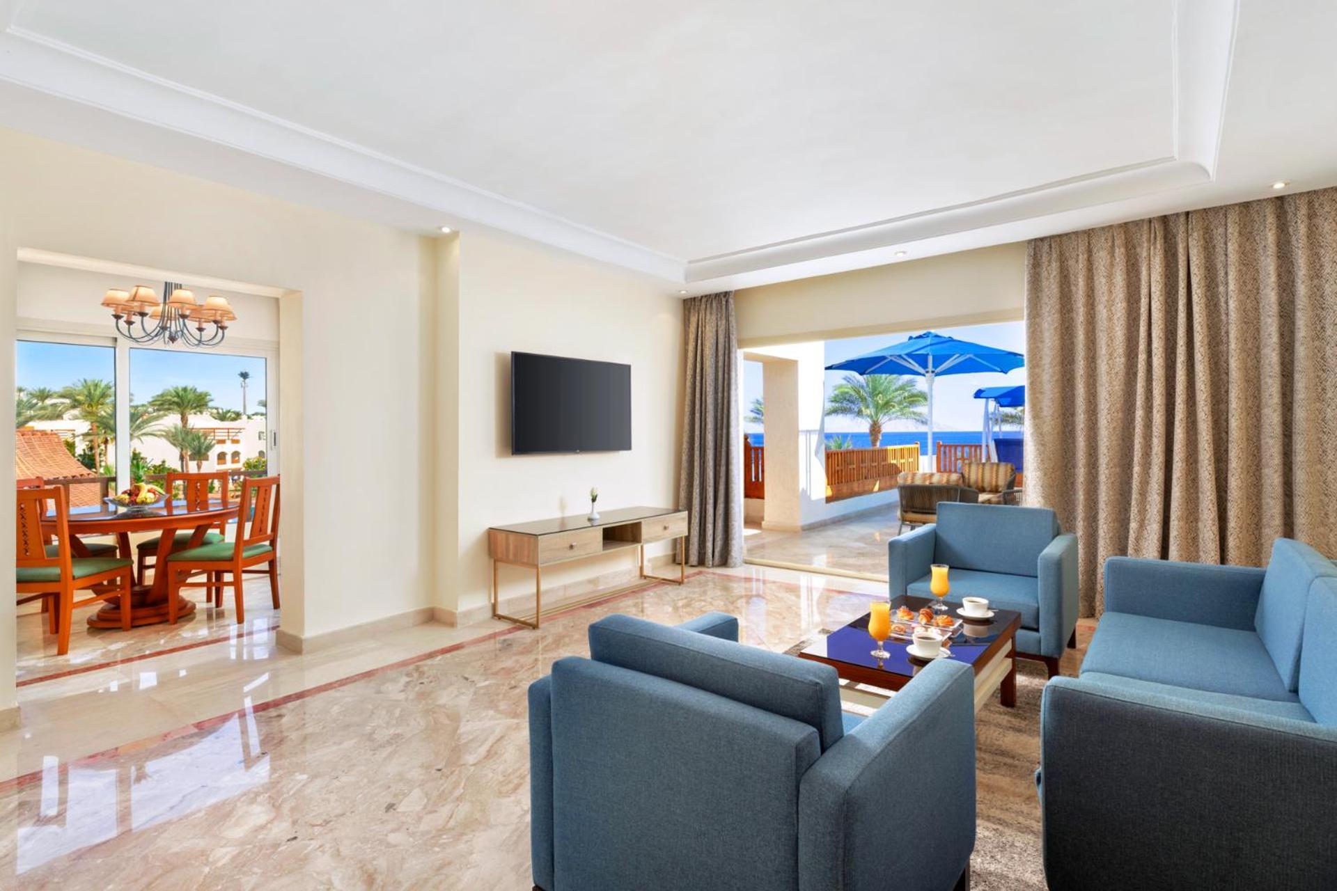 Pickalbatros Royal Grand Sharm - Adults Friendly 16 Years Plus Екстериор снимка The photo shows a modern and spacious living area. There are several blue chairs arranged around a coffee table, which holds some refreshments. A large flat-screen TV is mounted on the wall, and there are sliding glass doors that open to an outdoor a