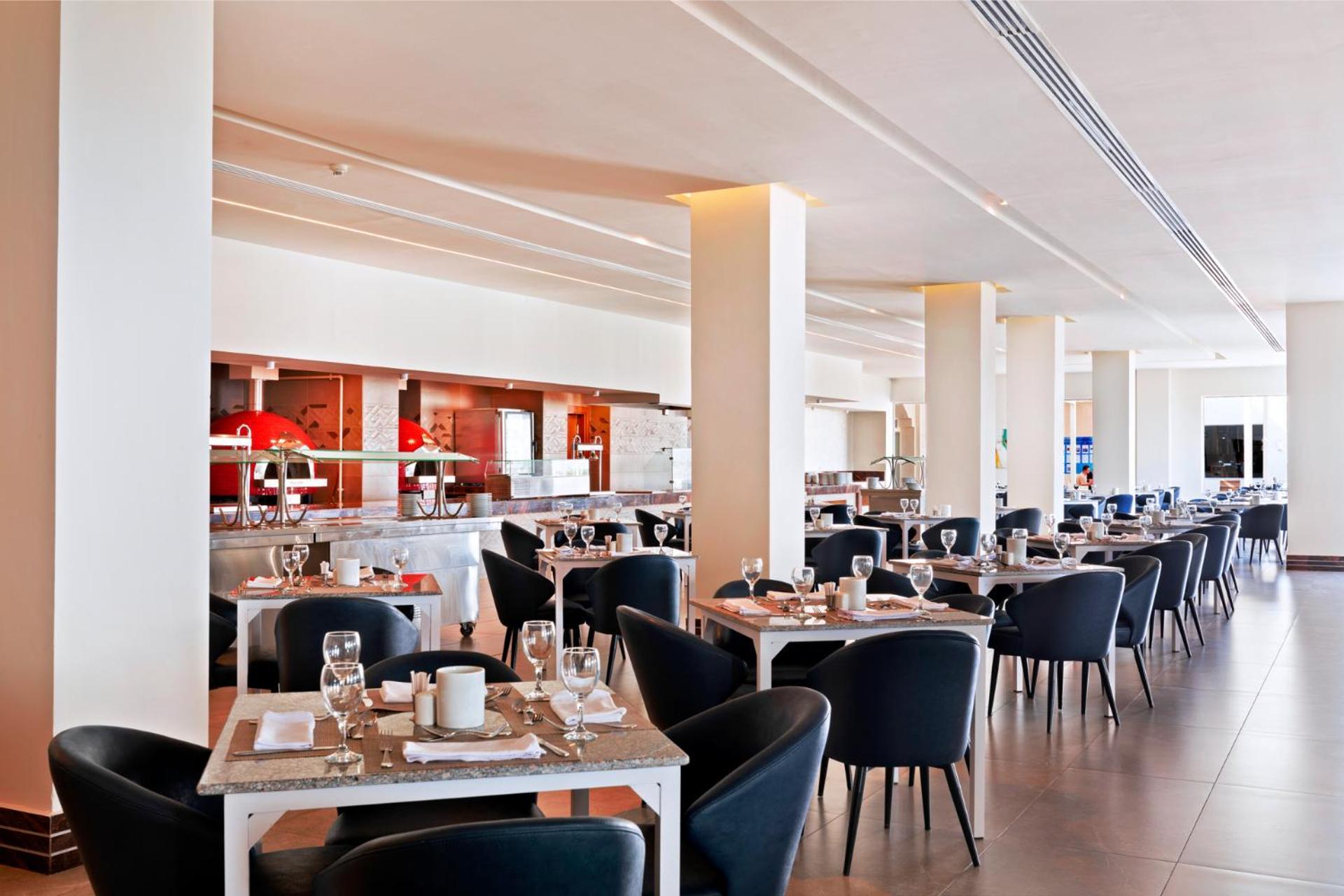 Pickalbatros Royal Grand Sharm - Adults Friendly 16 Years Plus Екстериор снимка The photo shows a modern restaurant interior. It features a spacious layout with several dining tables arranged in a row, each set with dishes, glasses, and cutlery. The tables have light-colored surfaces and are accompanied by black chairs. In the b