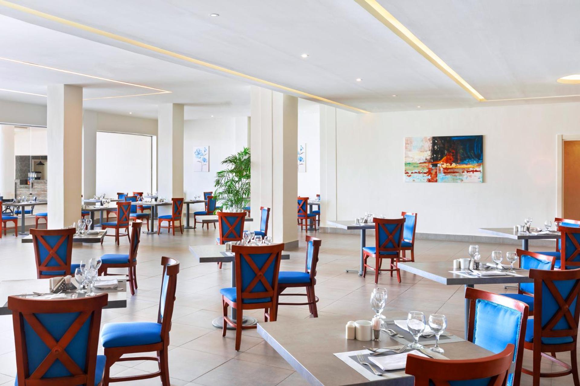 Pickalbatros Royal Grand Sharm - Adults Friendly 16 Years Plus Екстериор снимка The photo shows an interior of a restaurant featuring a modern and spacious design. The floors are tiled, and the walls are painted in neutral tones. The seating consists of wooden chairs with blue cushions arranged around tables, which are set with 