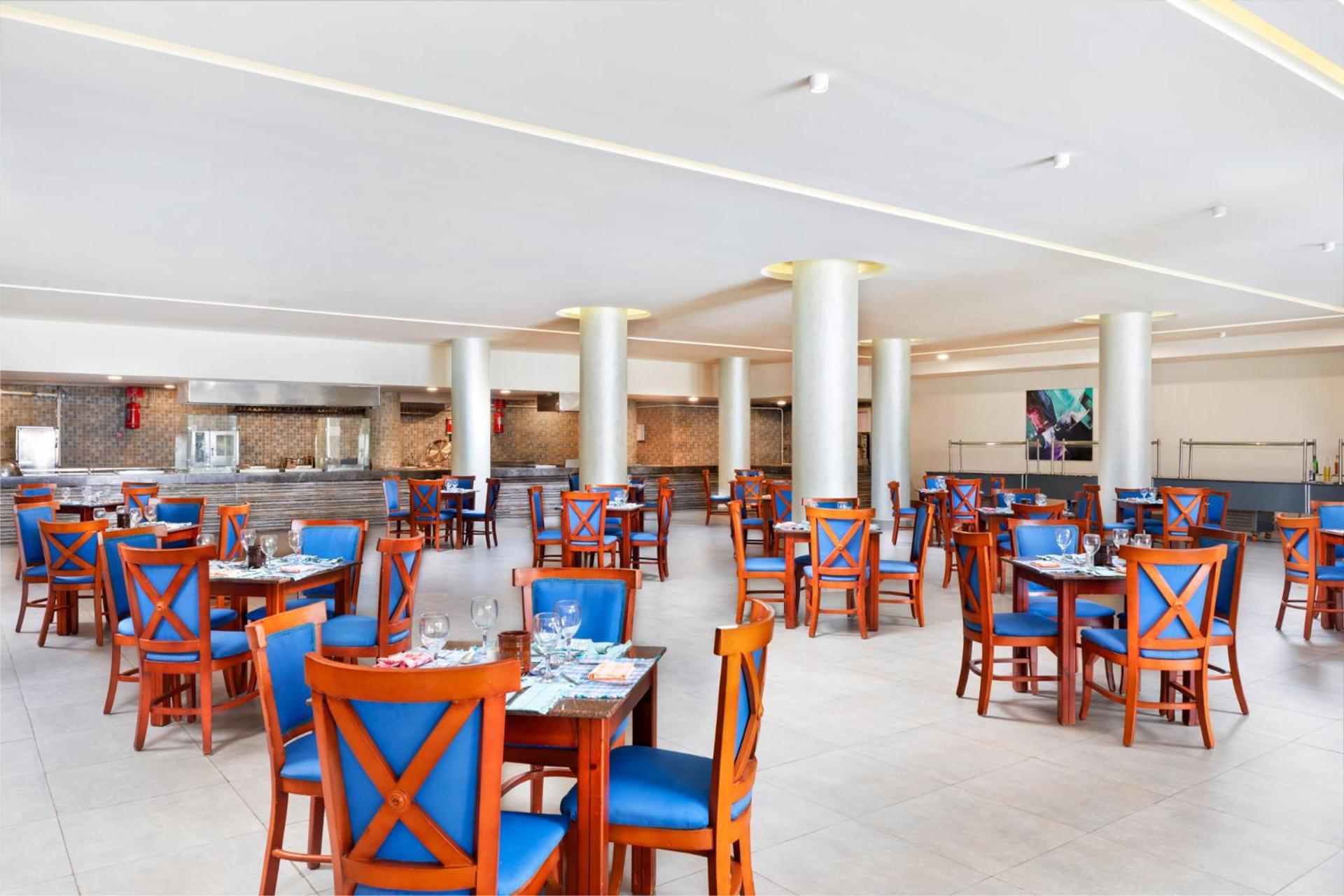 Pickalbatros Royal Grand Sharm - Adults Friendly 16 Years Plus Екстериор снимка The photo depicts a spacious dining area in a restaurant. The room features several wooden tables, each with blue chairs. The chairs have a unique design with prominent X-shaped backs. The flooring is light-colored tile, and the walls are painted in 