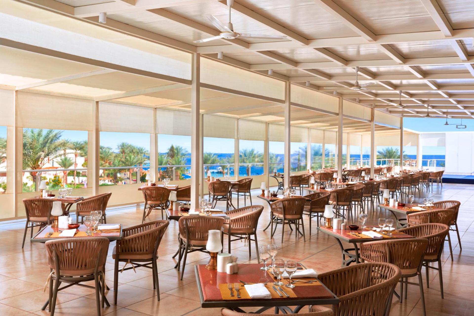 Pickalbatros Royal Grand Sharm - Adults Friendly 16 Years Plus Екстериор снимка The photo shows a spacious dining area in a restaurant with a modern and airy design. It features numerous wooden tables set with glasses and cutlery, arranged in a way that gives an open feel. Large windows provide a view of the outside, showcasing 