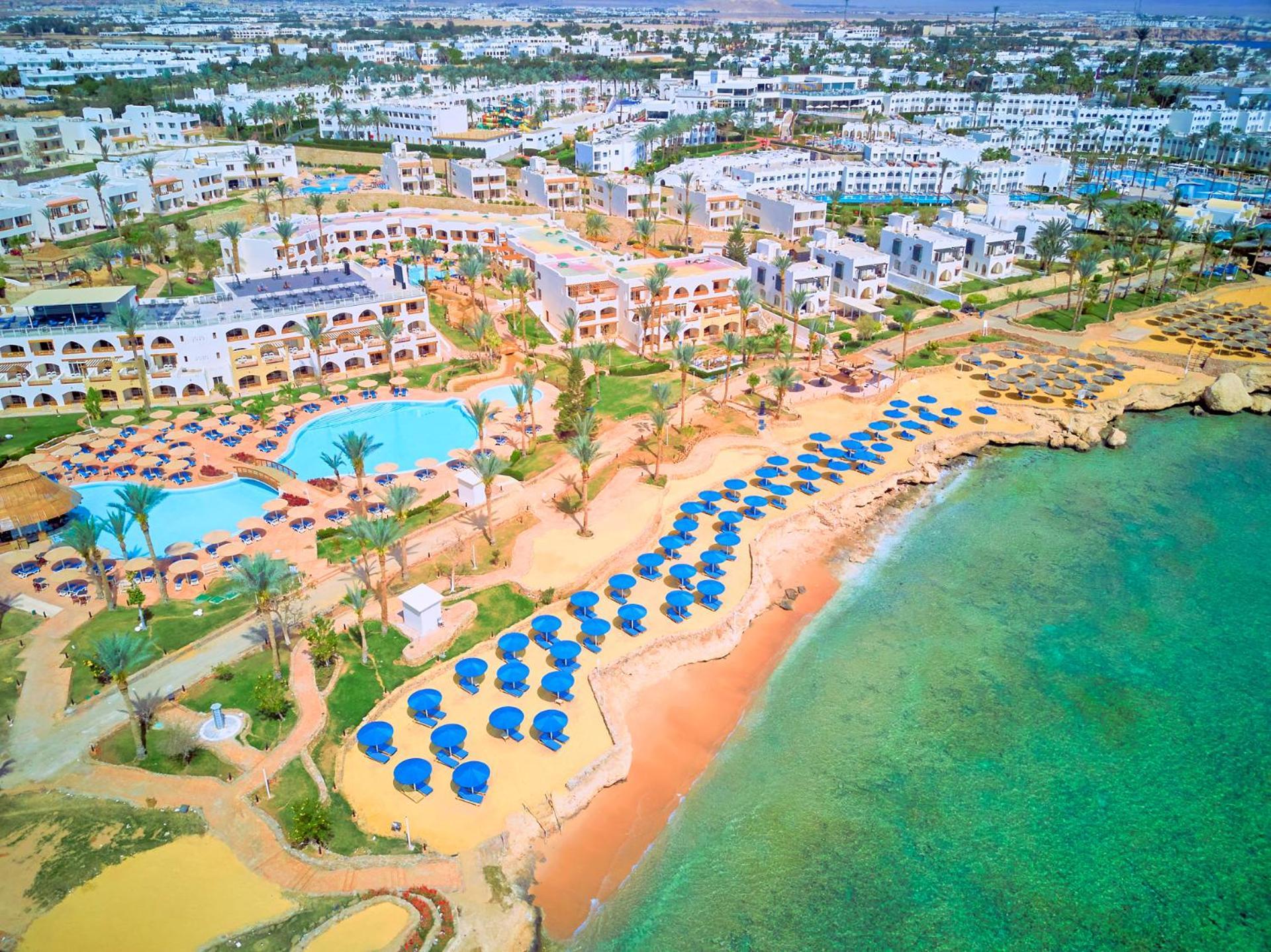 Pickalbatros Royal Grand Sharm - Adults Friendly 16 Years Plus Екстериор снимка The image shows an aerial view of a resort area by the beach. There is a swimming pool in the center, surrounded by palm trees and sun loungers. The sandy beach features numerous umbrellas arranged in rows for shade. In the background, there are seve