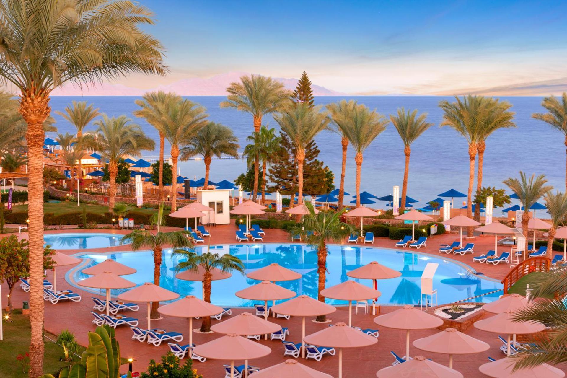 Pickalbatros Royal Grand Sharm - Adults Friendly 16 Years Plus Екстериор снимка The photo shows a beautiful resort scene with a swimming pool surrounded by lounge chairs and umbrellas. Palm trees line the area, adding to the tropical atmosphere. In the background, there is a view of the sea under a clear sky, suggesting a peacef