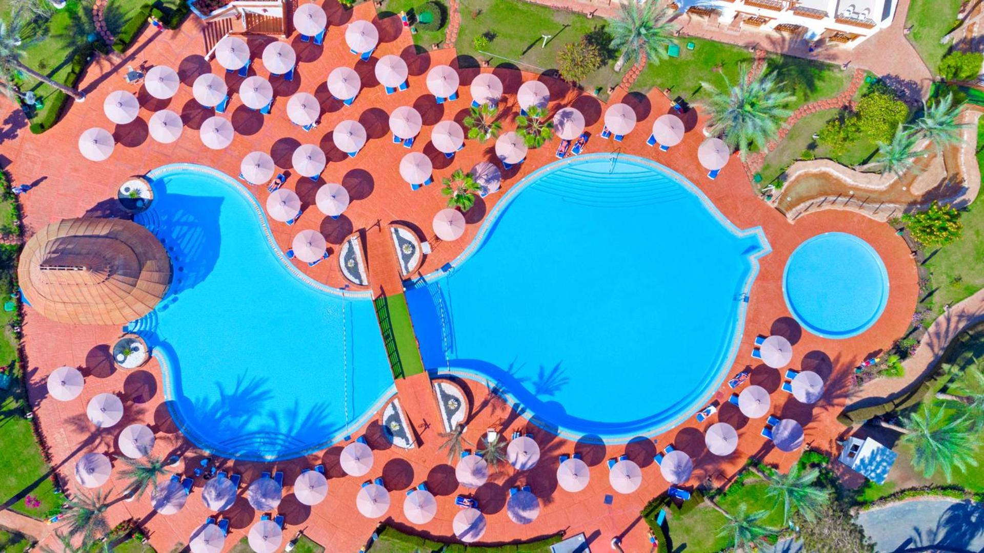 Pickalbatros Royal Grand Sharm - Adults Friendly 16 Years Plus Екстериор снимка The photo shows an aerial view of a large swimming pool area, shaped in a distinctive layout resembling two interconnected pools. Surrounding the main pool are numerous umbrellas, providing shade for visitors. The pool area is set on a reddish-colore