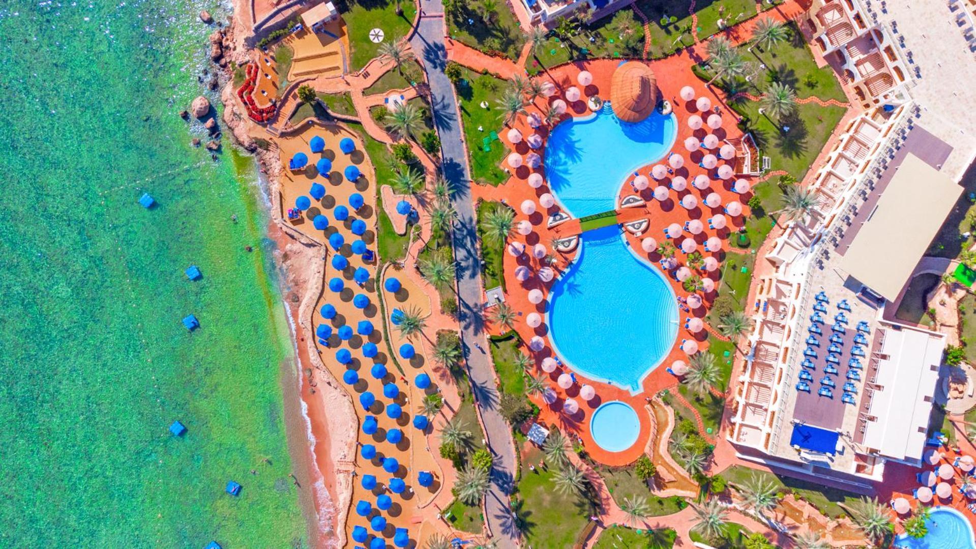 Pickalbatros Royal Grand Sharm - Adults Friendly 16 Years Plus Екстериор снимка The photo shows an aerial view of a beach resort. In the foreground, there's a large swimming pool shaped like a flowing river, surrounded by lounge chairs and umbrellas. The pool has a distinctive, organic design with curved edges. To the left, ther