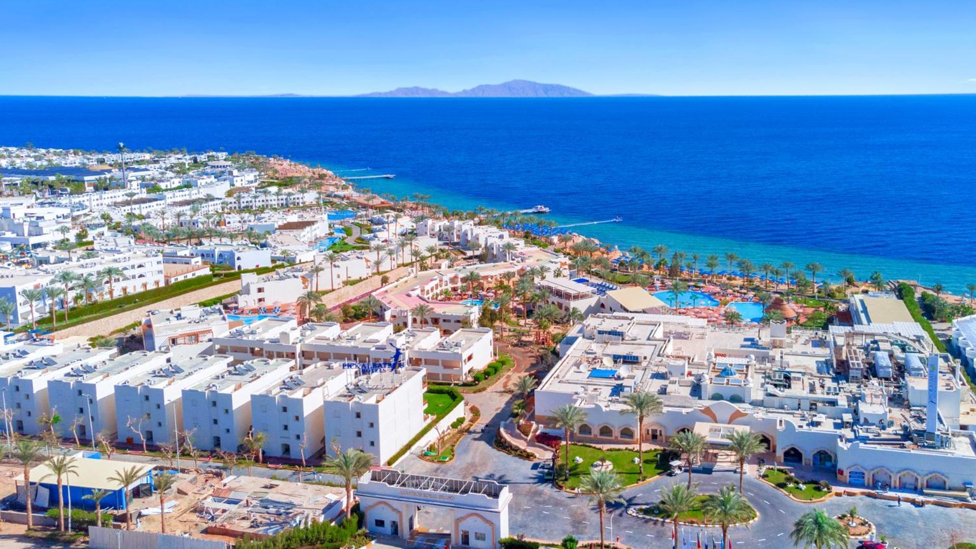 Pickalbatros Royal Grand Sharm - Adults Friendly 16 Years Plus Екстериор снимка The photo shows a beautiful coastal landscape, featuring a resort area by the sea. There are white buildings, likely hotels or villas, arranged in a sprawling layout near the beach. The water is a vibrant blue, contrasting with the sandy shore and gr
