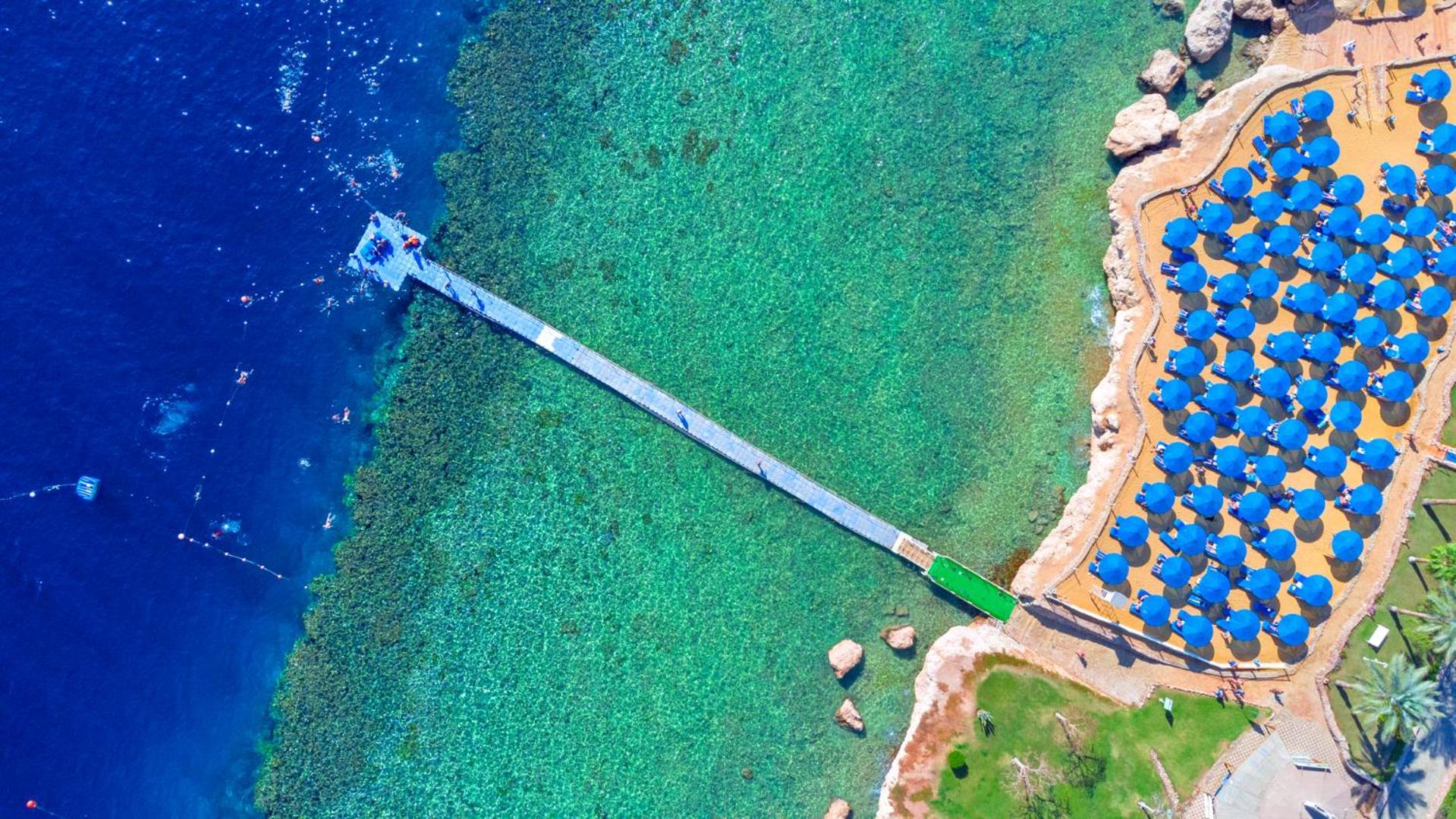 Pickalbatros Royal Grand Sharm - Adults Friendly 16 Years Plus Екстериор снимка The photo shows an aerial view of a coastal area featuring a long wooden pier extending into clear turquoise water. On one side of the pier, there appears to be a beach with umbrellas or sunbeds arranged neatly. The water is vibrant and visually invi