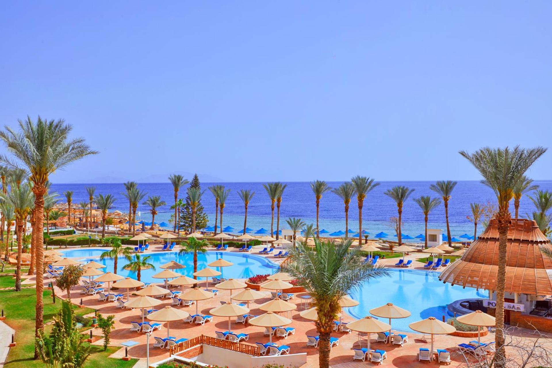 Pickalbatros Royal Grand Sharm - Adults Friendly 16 Years Plus Екстериор снимка The photo showcases a beautiful resort setting by the sea. It features a large swimming pool surrounded by sunny lounge chairs and umbrellas, perfect for relaxation. The area is adorned with lush palm trees, adding to the tropical vibe. In the backgr