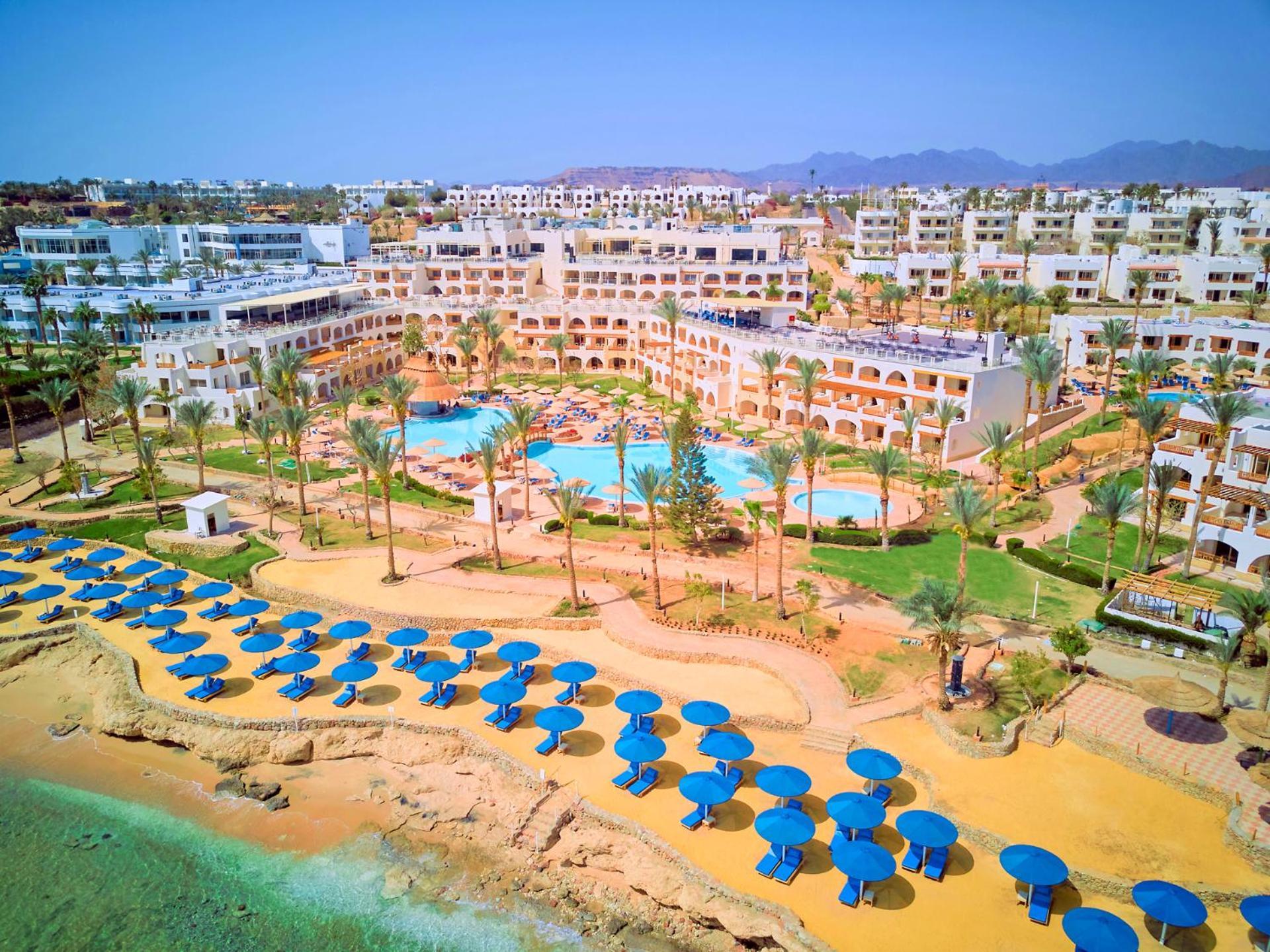 Pickalbatros Royal Grand Sharm - Adults Friendly 16 Years Plus Екстериор снимка The photo shows a vibrant resort area with several buildings that appear to be accommodations or hotel units. There are multiple swimming pools surrounded by palm trees, creating a tropical atmosphere. In the foreground, there is a beach area with sa