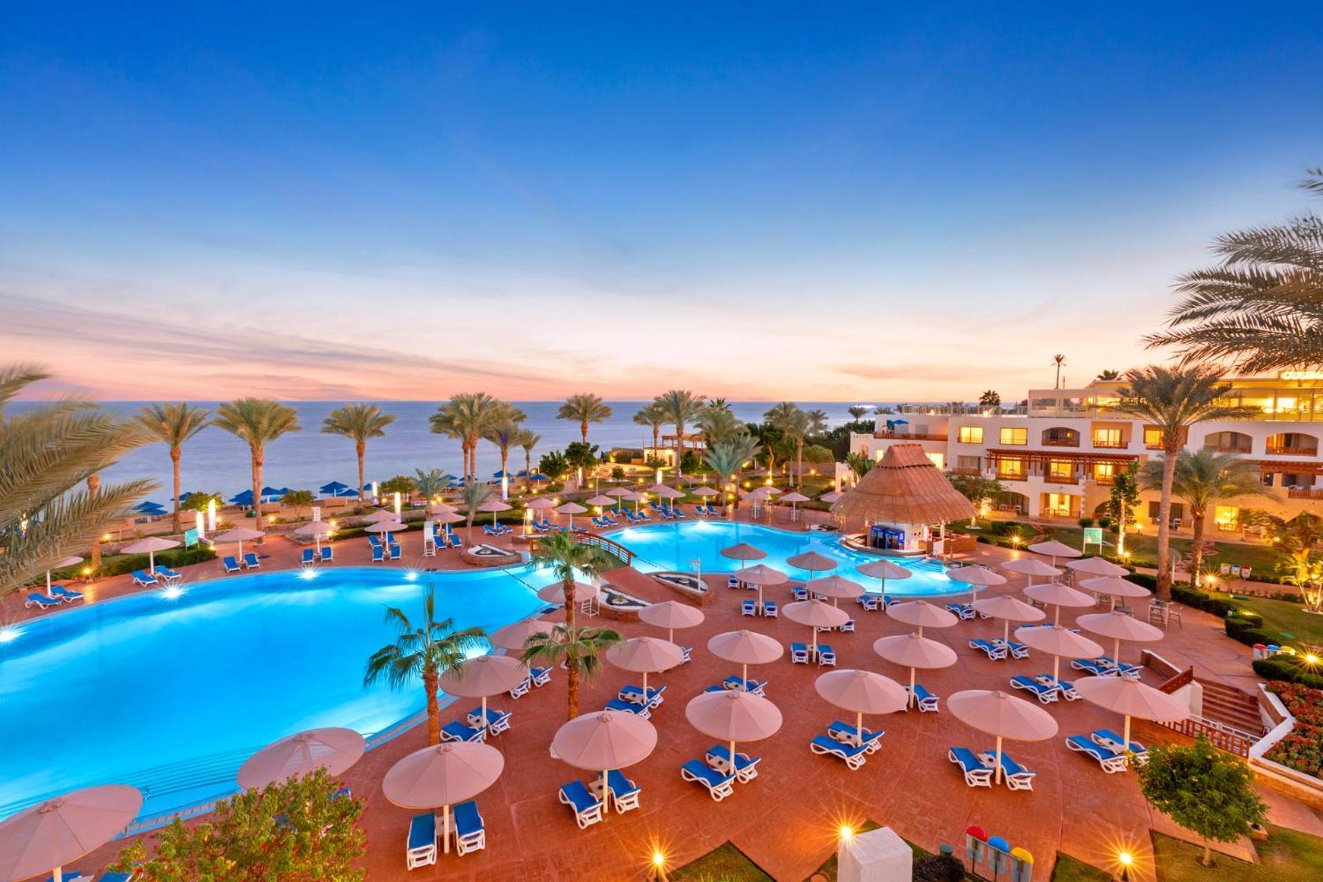 Pickalbatros Royal Grand Sharm - Adults Friendly 16 Years Plus Екстериор снимка The photo showcases a luxurious resort setting with two large swimming pools, surrounded by lounge chairs and umbrellas. Palm trees are interspersed around the pool area, enhancing the tropical feel. In the background, there’s a view of the ocean, an