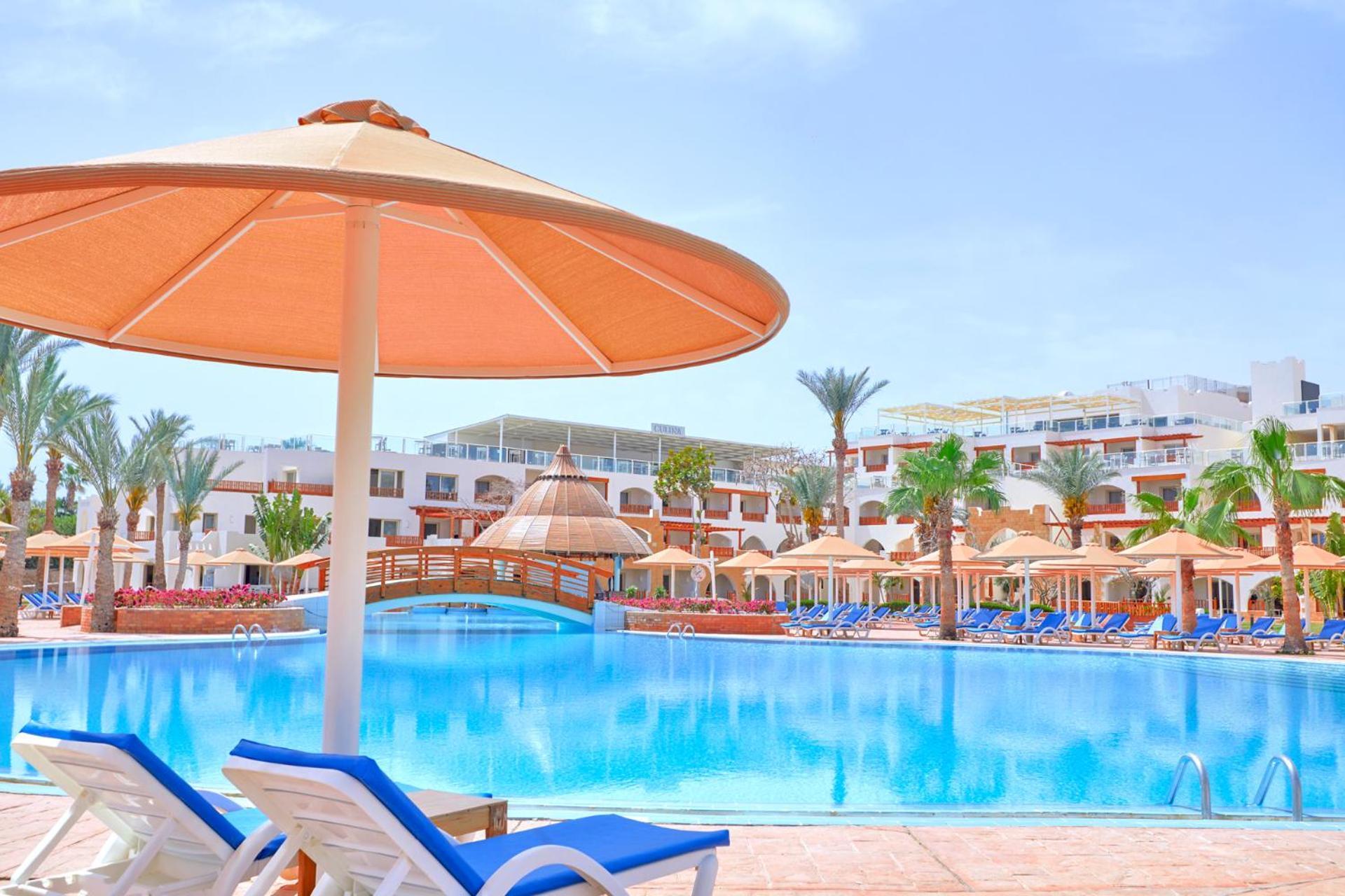 Pickalbatros Royal Grand Sharm - Adults Friendly 16 Years Plus Екстериор снимка The photo shows a picturesque resort scene featuring a large swimming pool surrounded by lounge chairs and umbrellas. The pool is shimmering under a bright blue sky, and there are several palm trees in the background, adding to the tropical atmospher