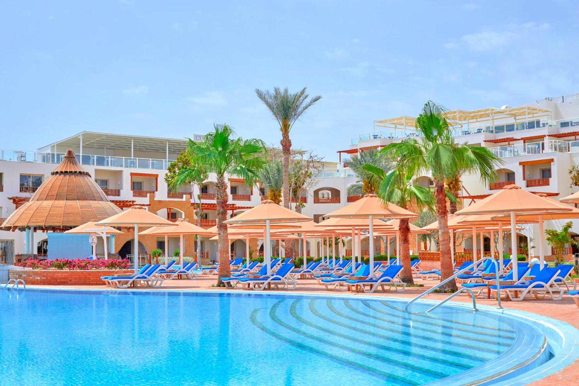 Pickalbatros Royal Grand Sharm - Adults Friendly 16 Years Plus Екстериор снимка The photo depicts a resort scene featuring a beautiful swimming pool with clear blue water. Surrounding the pool are several lounge chairs arranged under large umbrellas, providing shade. In the background, there are palm trees that enhance the tropi