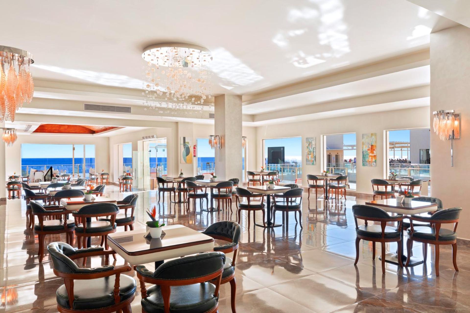 Pickalbatros Royal Grand Sharm - Adults Friendly 16 Years Plus Екстериор снимка The photo shows a bright and elegant restaurant interior. There are several tables arranged throughout the space, each with chairs around them. The decor features modern lighting, including a chandelier, and large windows that allow natural light to 
